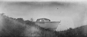 A boat sitting in the grass near some tall weeds.