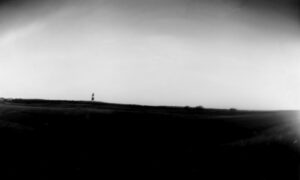 A black and white photo of a field with a lighthouse.
