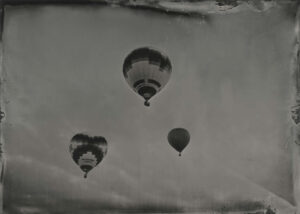 Three balloons flying in the sky with a cloudy background