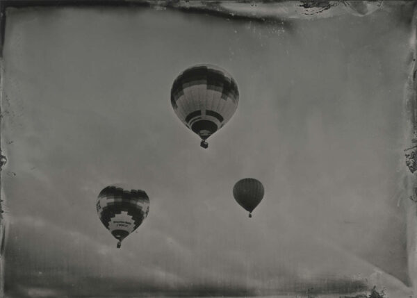 Three balloons flying in the sky with a cloudy background