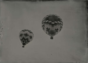 Two balloons flying in the sky with a cloudy background