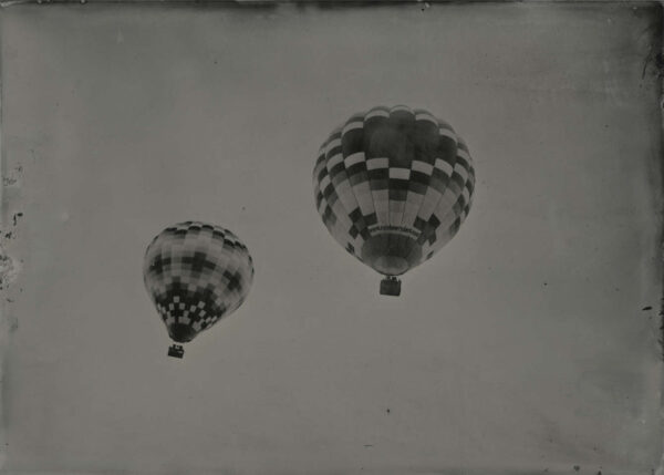 Two balloons flying in the sky with a cloudy background