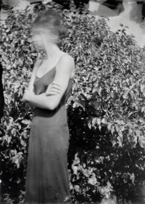 A woman in a dress standing next to bushes.