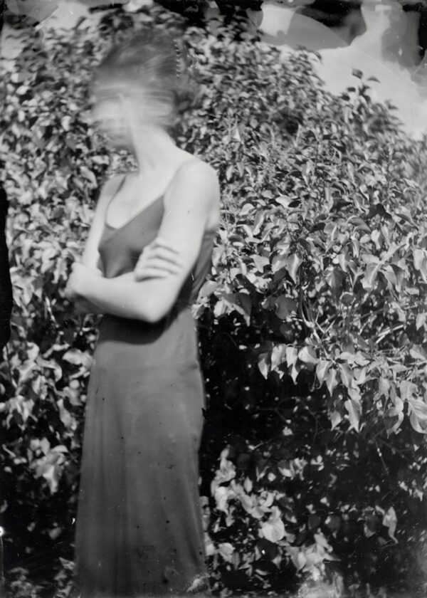 A woman in a dress standing next to bushes.