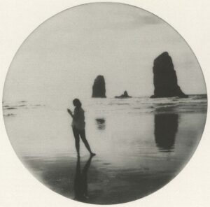 A woman standing on the beach with two rocks in the background.