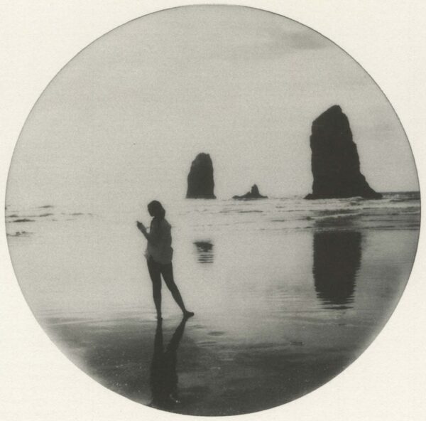A woman standing on the beach with two rocks in the background.