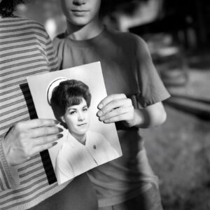 A woman holding up an old photo of herself.