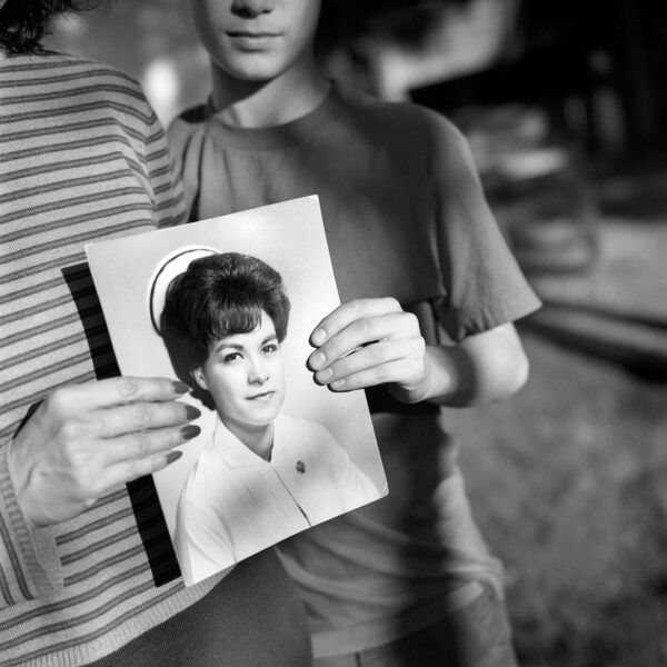 A woman holding up an old photo of herself.