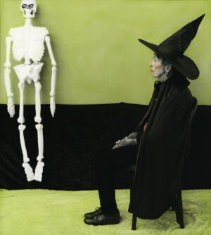 A person in costume sitting next to a skeleton.