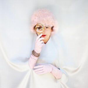 A woman in white dress and pink hat holding her hand to the side of her face.