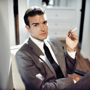 A man in a suit and tie holding a cigarette.