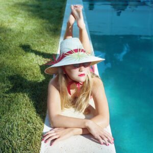 A woman in a hat laying on the edge of a pool.