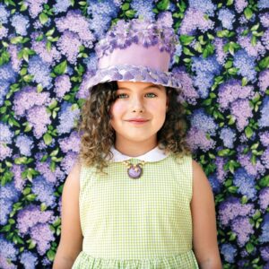 A girl wearing a hat and necklace in front of a floral background.