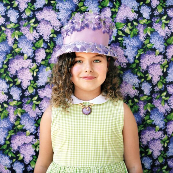 A girl wearing a hat and necklace in front of a floral background.