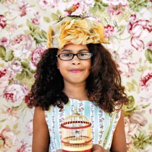 A girl with glasses and a floral headband holding a cake.
