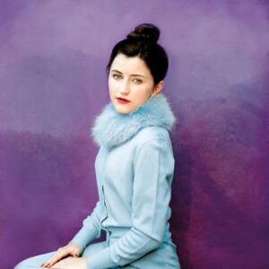 A woman in blue is sitting against a purple wall.