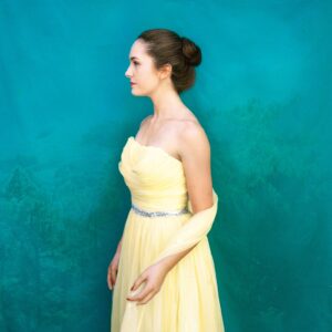 A woman in yellow dress standing next to wall.