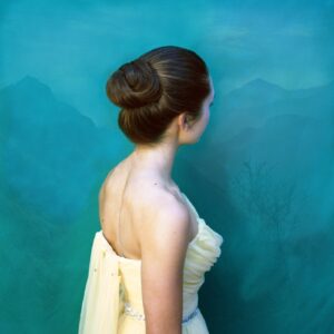 A woman in white dress standing next to a blue wall.