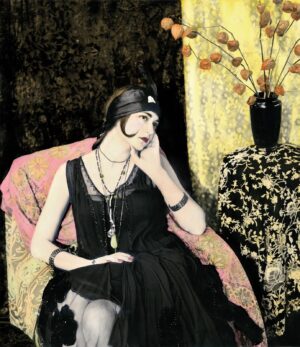 A woman in black dress sitting on chair talking on phone.