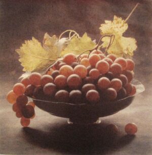 A bowl of grapes with leaves on the table.