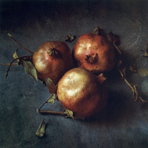 Three pomegranates on a table with leaves.