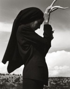 A woman in black suit and head covering holding her hand up.