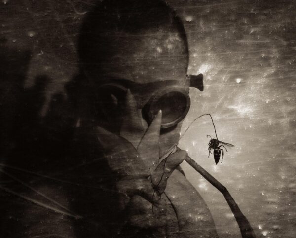 A man with a skull face and spider in the background.