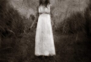 A woman in white dress standing on grass.