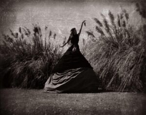 A woman in black dress standing next to tall grass.