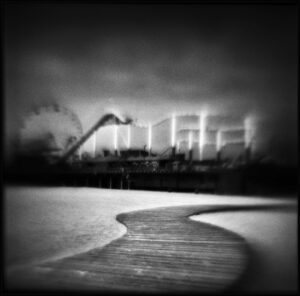 A black and white photo of the ocean with a ferris wheel in the background.