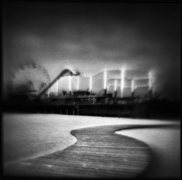 A black and white photo of the ocean with a ferris wheel in the background.