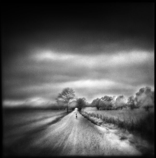 A black and white photo of a road with trees in the background.