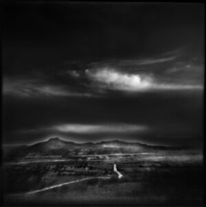 A black and white photo of a field with clouds in the sky.