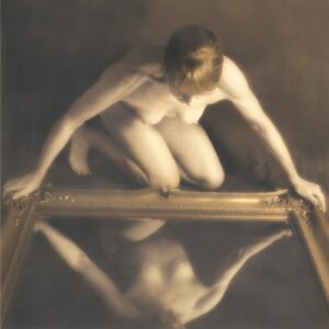 A man is sitting on the ground and looking at his reflection in water.