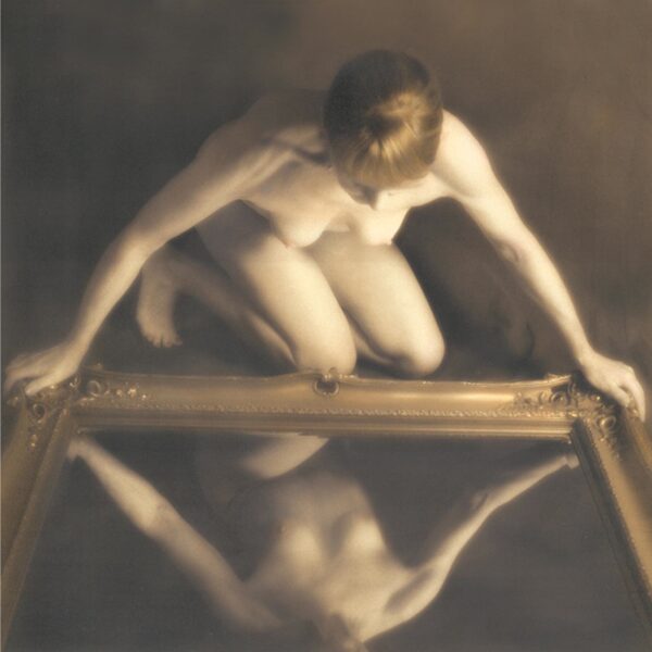 A man is sitting on the ground and looking at his reflection in water.