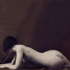 A naked woman laying on the ground in front of a wall.