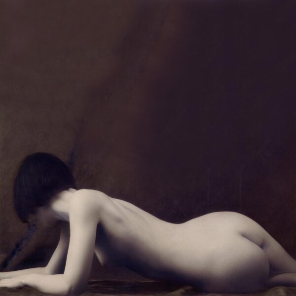 A naked woman laying on the ground in front of a wall.