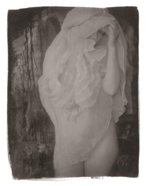 A woman in a white dress standing next to a tree.