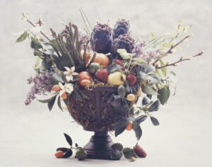 A bowl of fruit and flowers on top of a table.