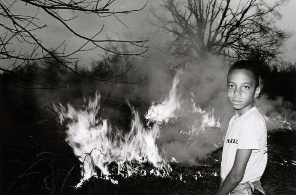 A young boy standing in front of fire.
