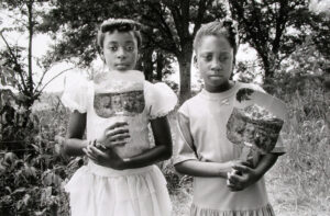 Two young girls holding baskets in a park.