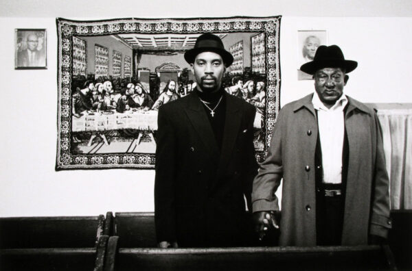 Two men in hats and suits standing next to a painting.