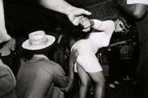 A woman in white dress and hat dancing with two men.