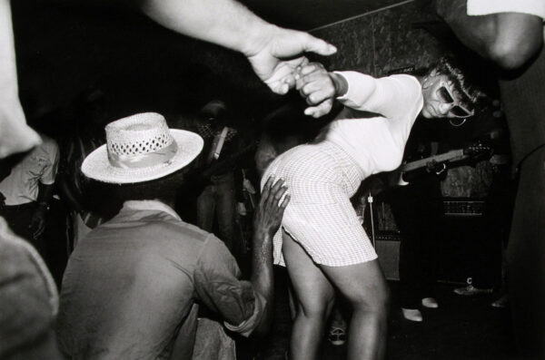 A woman in white dress and hat dancing with two men.