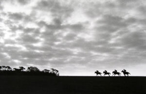 A black and white photo of horses running in the distance.