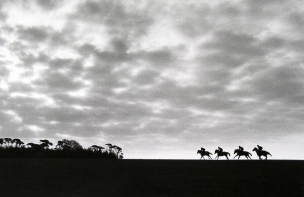 A black and white photo of horses running in the distance.