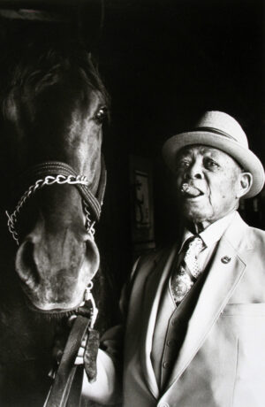 A man in suit and hat next to horse.