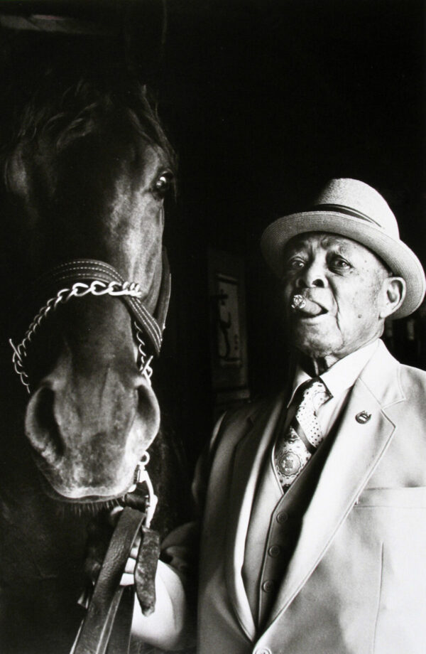 A man in suit and hat next to horse.