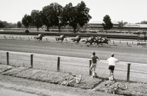 Two men standing on a dirt road watching horses.