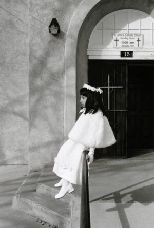 A young girl in white dress sitting on the steps of a church.